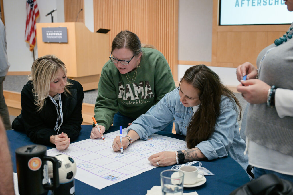 Three women writing on a large piece of paper.